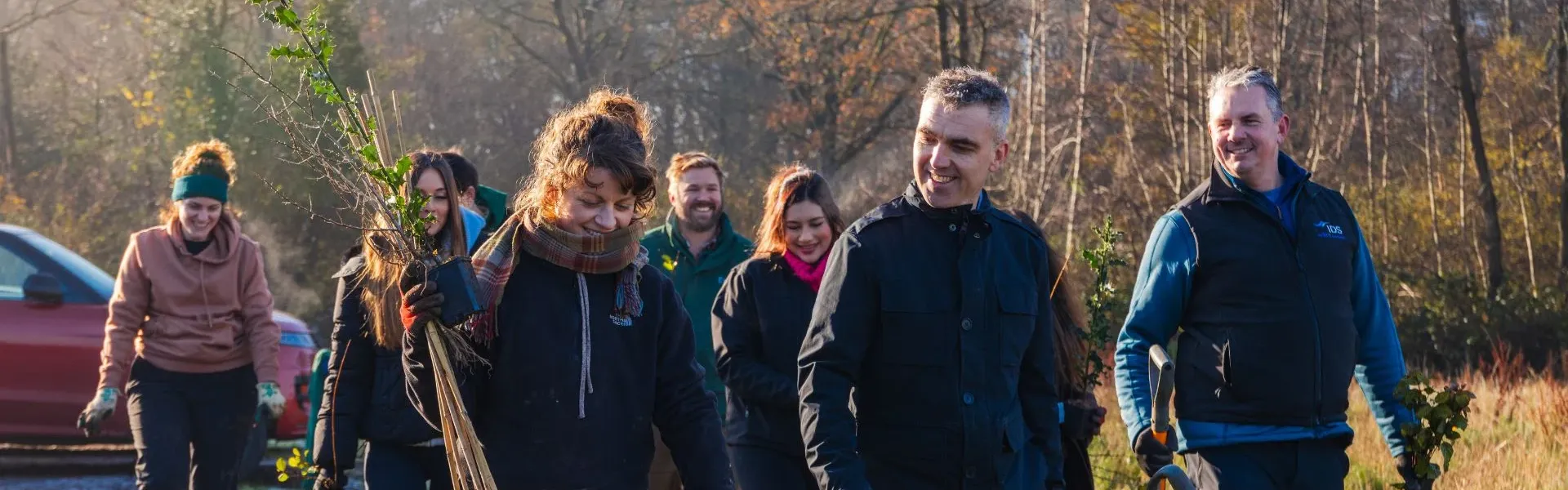 Photograph: Volunteers carrying saplings, walking on a dirt track to plant trees.